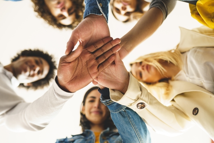 Migration and resettlement image A photo of a group of people stood in a circle from below, with their hands together in the middle of the circle.